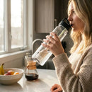 Woman drinking from a water bottle in a kitchen with FlavaFil cleaning her water
